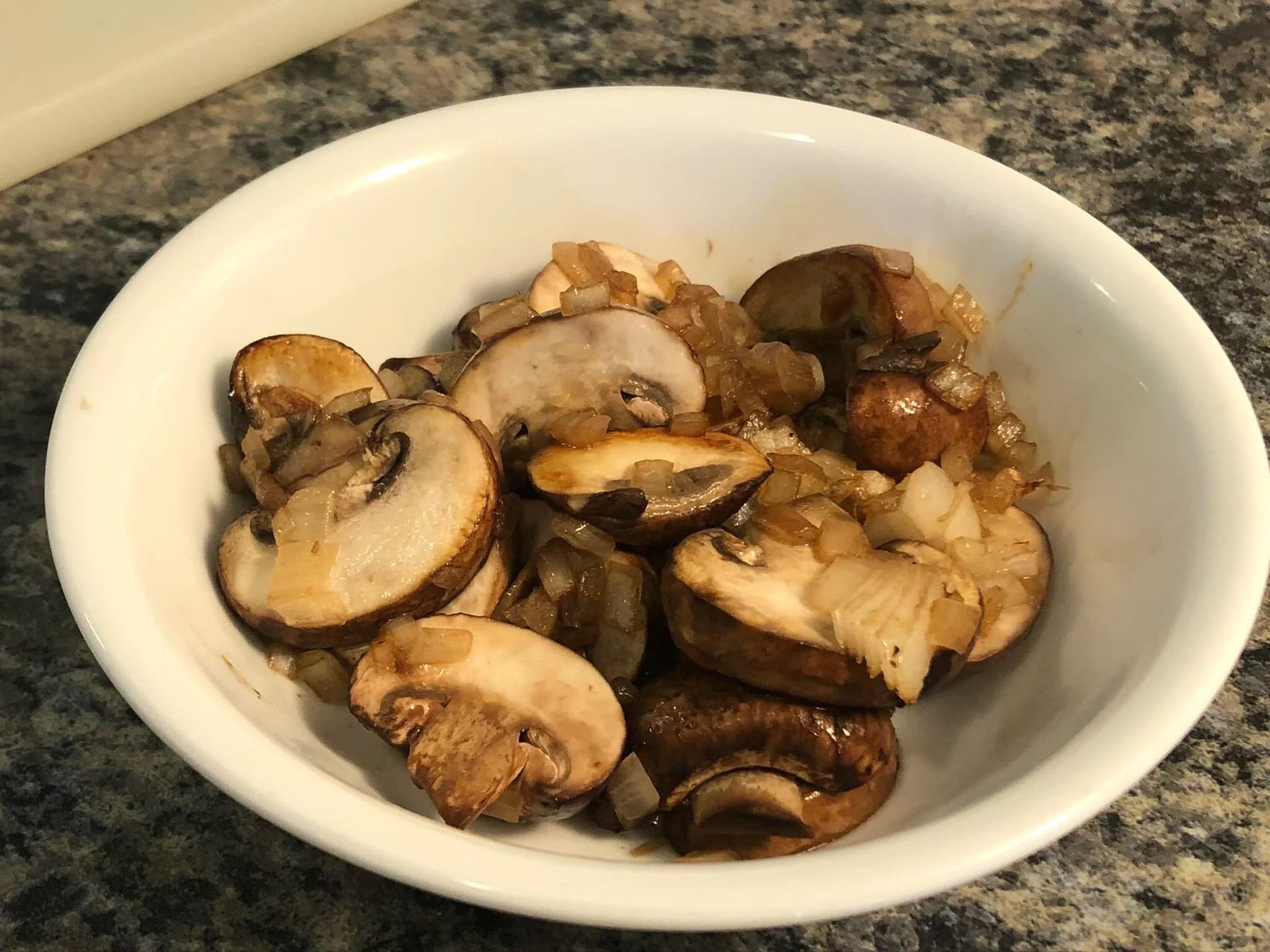 Sautéed sliced mushrooms and diced onions in a white bowl, cooked until golden brown.