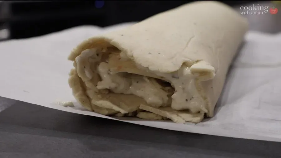 Gluten-free strukli dough rolled into a tight log with cheese filling visible inside, on parchment paper.