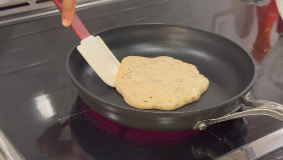 Pouring chocolate chip cookie pancake batter onto a non-stick skillet with a spatula.
