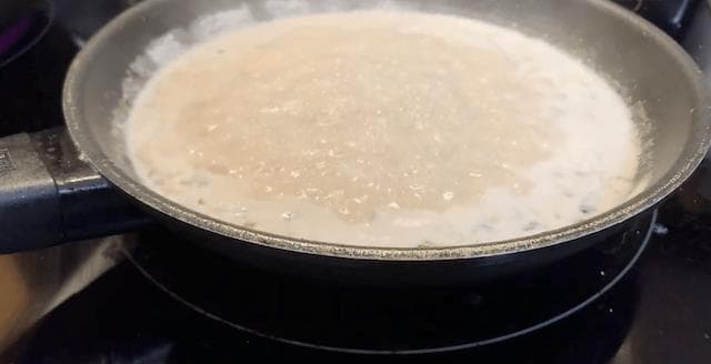 Creamy coconut milk sauce simmering in a dark pan on the stovetop