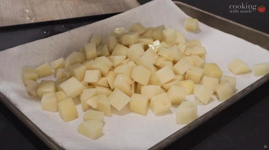 Diced potatoes coated with olive oil spread on a white paper-lined tray, ready for air frying.