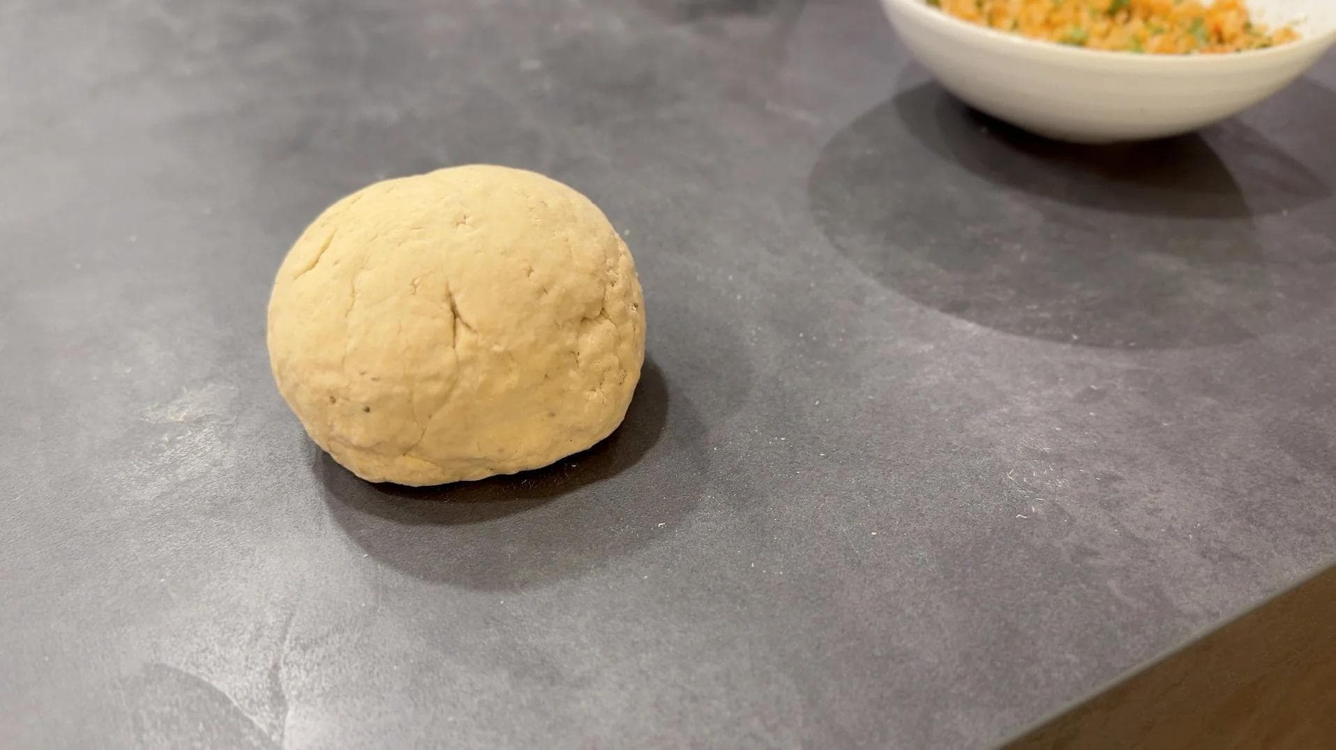 Smooth ball of rested paratha dough on a dark work surface, ready to be rolled out.