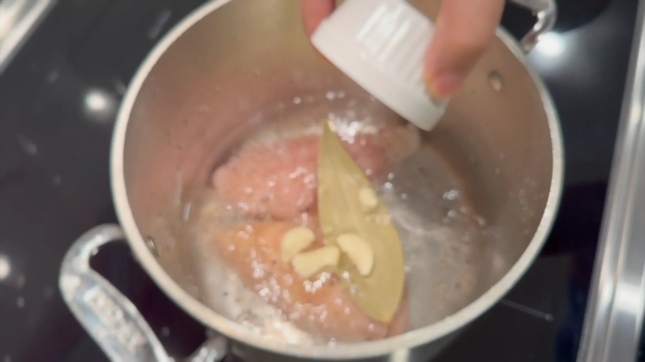 Salt being added to a pot of raw chicken breasts and water for poaching.