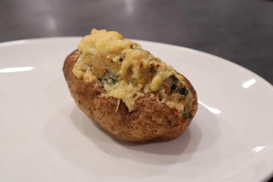 Crispy baked potato skin topped with fluffy mashed potato filling and melted butter on a white plate.