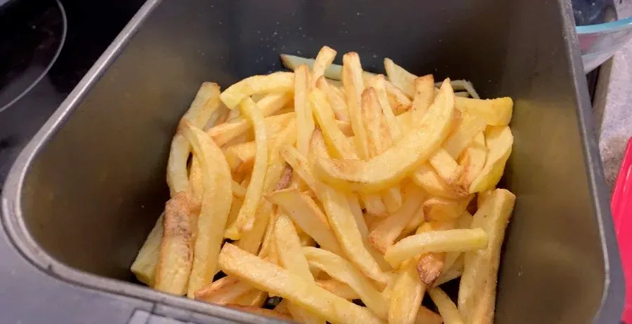 Crispy golden air fryer fries in a basket, ready to be tossed with garlic parmesan coating.