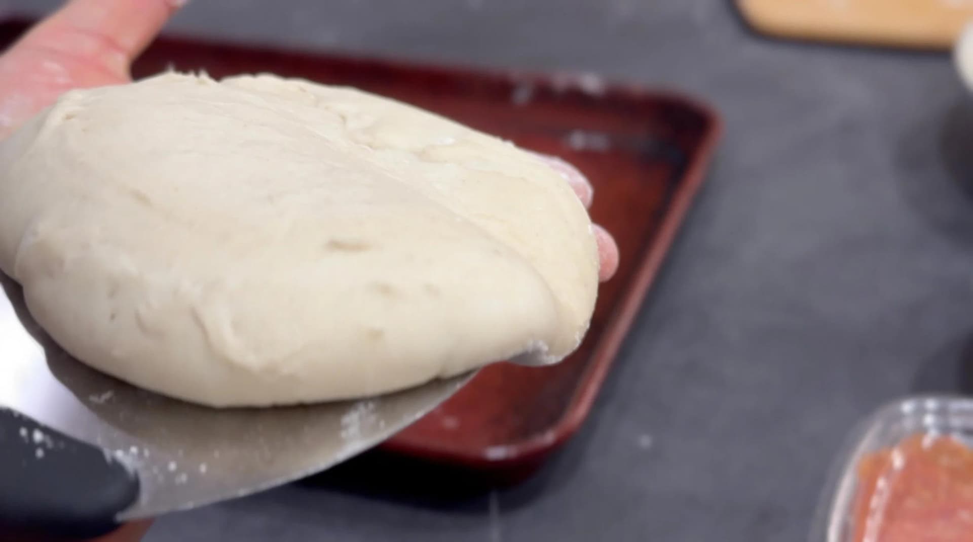 Hand holding stretched pizza dough ball over flour-dusted counter before shaping