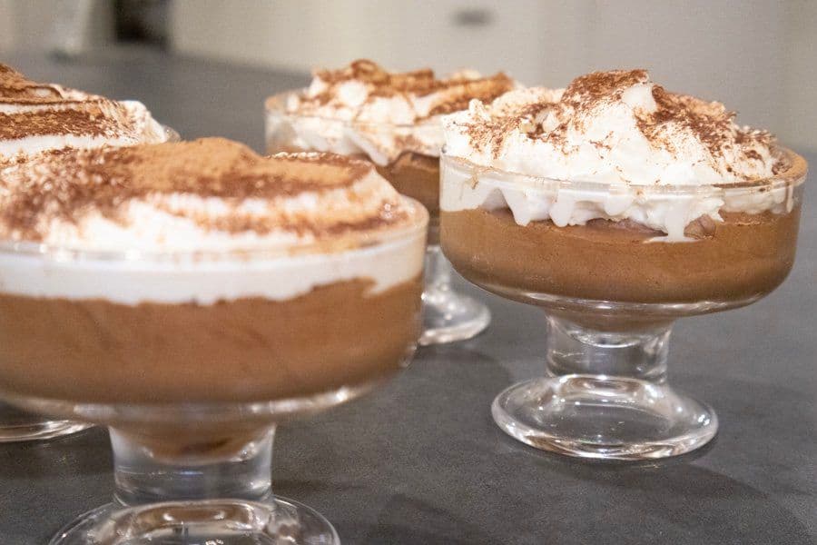 Chocolate mousse desserts in glass bowls topped with whipped cream and cocoa powder