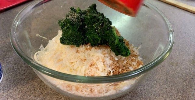 Spinach dip ingredients mixed in a glass bowl with fresh spinach on top before combining.