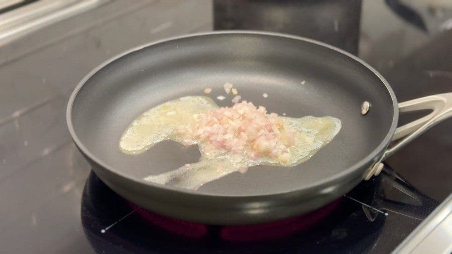 Butter and diced shallots sautéing in a non-stick pan on stovetop.