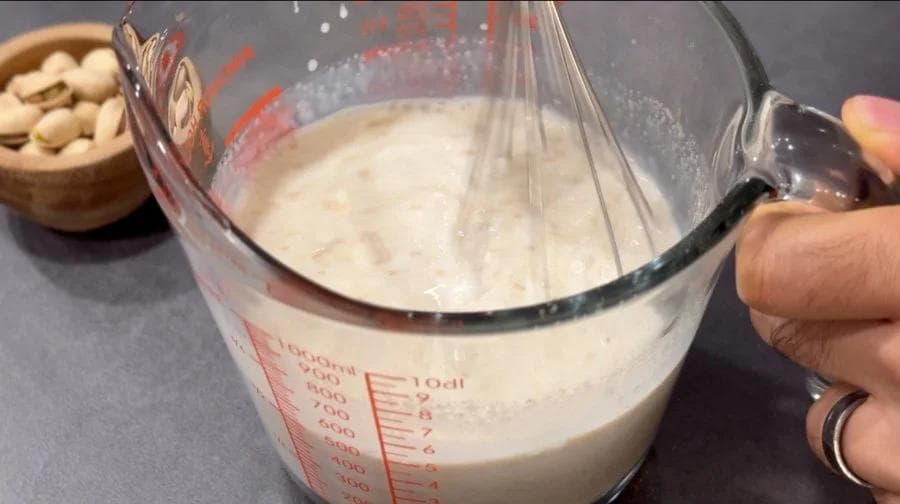 Whisking condensed milk and spice mixture in a measuring bowl with a whisk for Sooji Kheer ice cream.