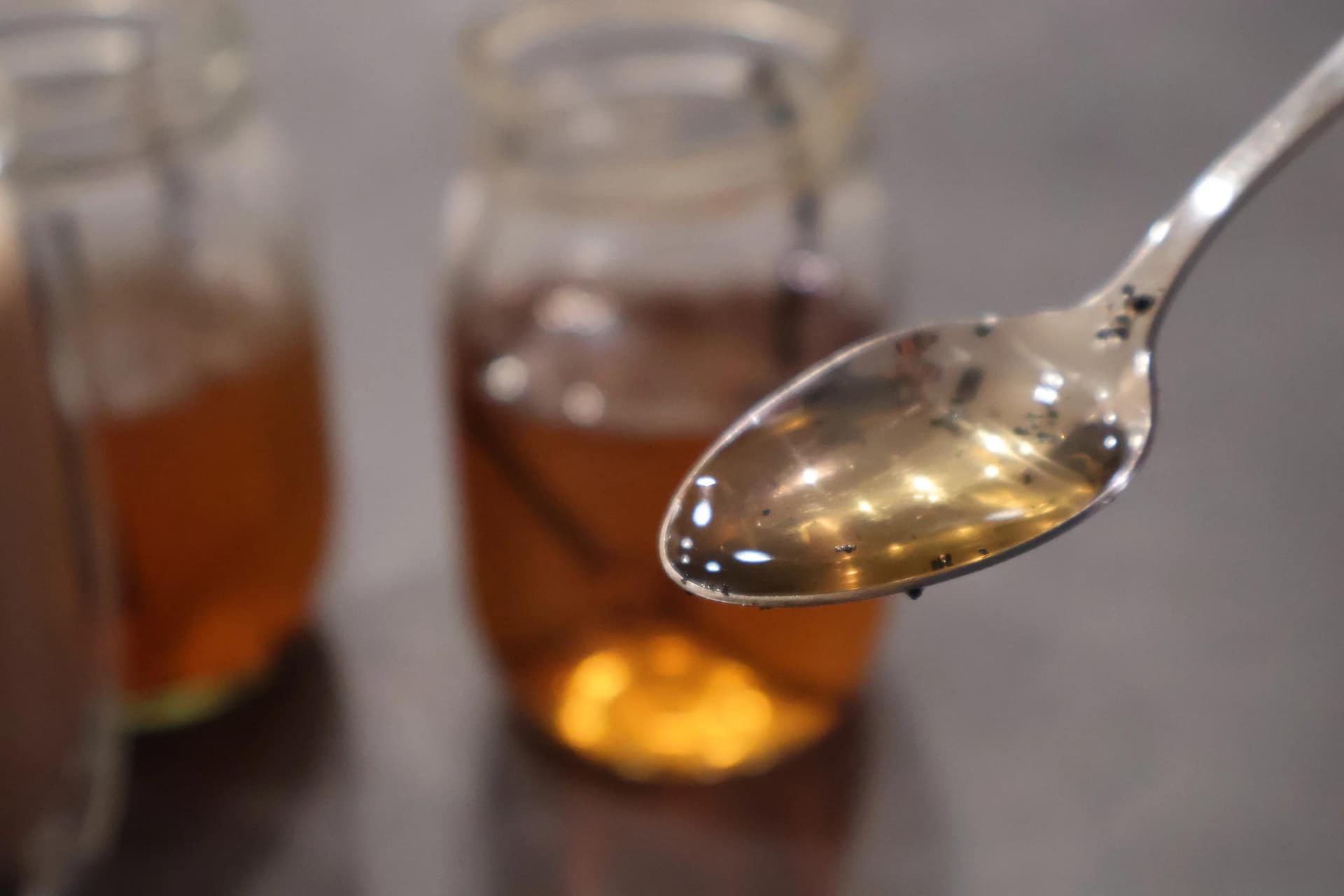 Homemade vanilla syrup dripping from a spoon over glass jars containing the amber-colored syrup.