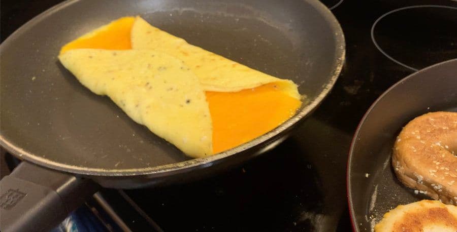 Folded omelette with melted cheese in the center cooking in a non-stick pan on the stovetop.