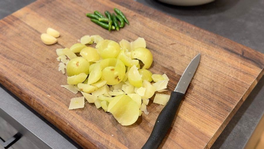 Sliced amla pieces on a wooden cutting board with a knife and chopped green chillies nearby.