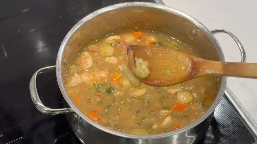Simmering country harvest chicken stew in a pot with vegetables, being stirred with a wooden spoon.