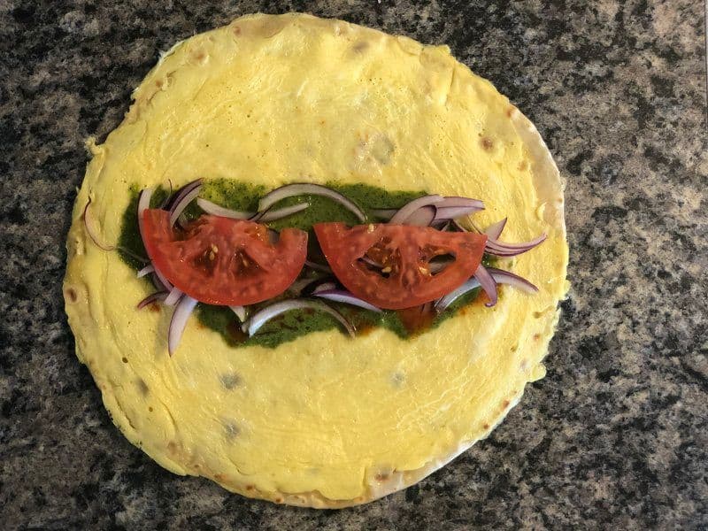 Yellow paratha with sliced tomatoes, onions, and lettuce arranged in the center before wrapping into a kathi roll.