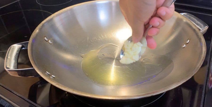 Hand adding diced onions to hot oil and butter in a wok on a stovetop.