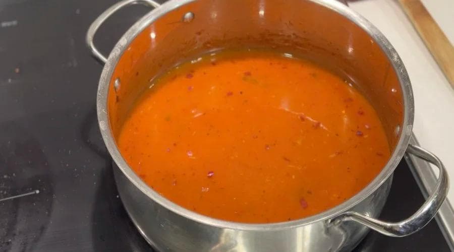 Orange tomato-based broth simmering in a stainless steel pot on a stovetop.