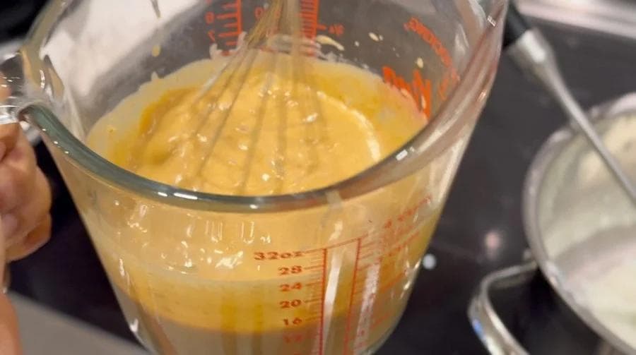 Creamy pumpkin custard mixture being whisked in a measuring cup during tempering process.