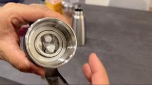 Hand holding open whipped cream dispenser head showing inserted gasket and metal tip.