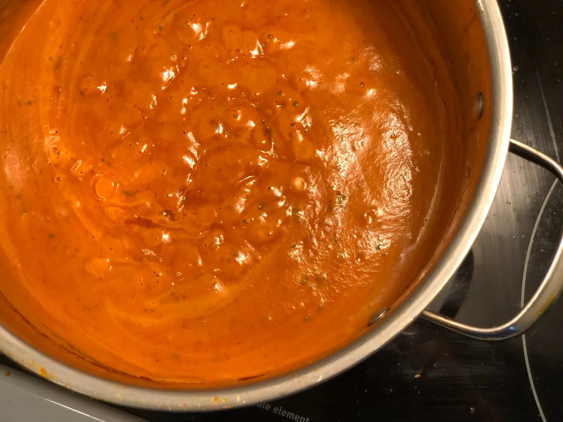 Bubbling orange butter chicken makhani sauce simmering in a pot on a stovetop.