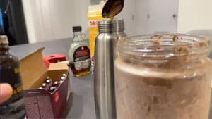 Whipped cream dispenser with cream mixture and charger being inserted into metal canister on kitchen counter.