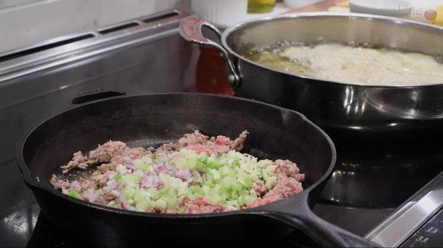 Ground meat and vegetable mixture being sautéed in a black skillet with diced shallots and green onions.