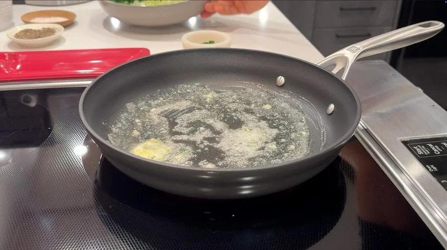 Leeks and kale wilting in garlic-chive butter in a black skillet over medium heat.