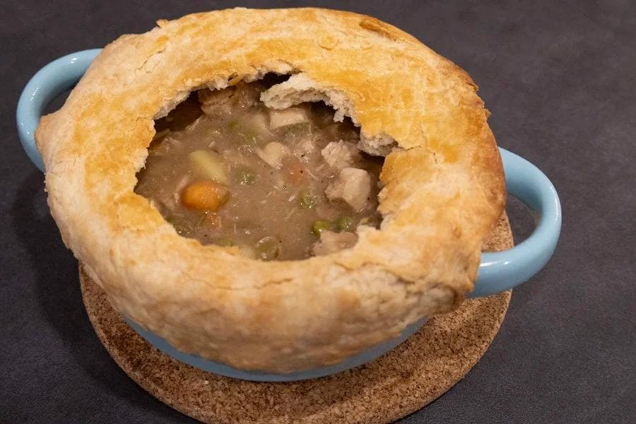 Guinness chicken pot pie in a blue ceramic dish with golden pastry crust, showing creamy filling with vegetables visible through opening.