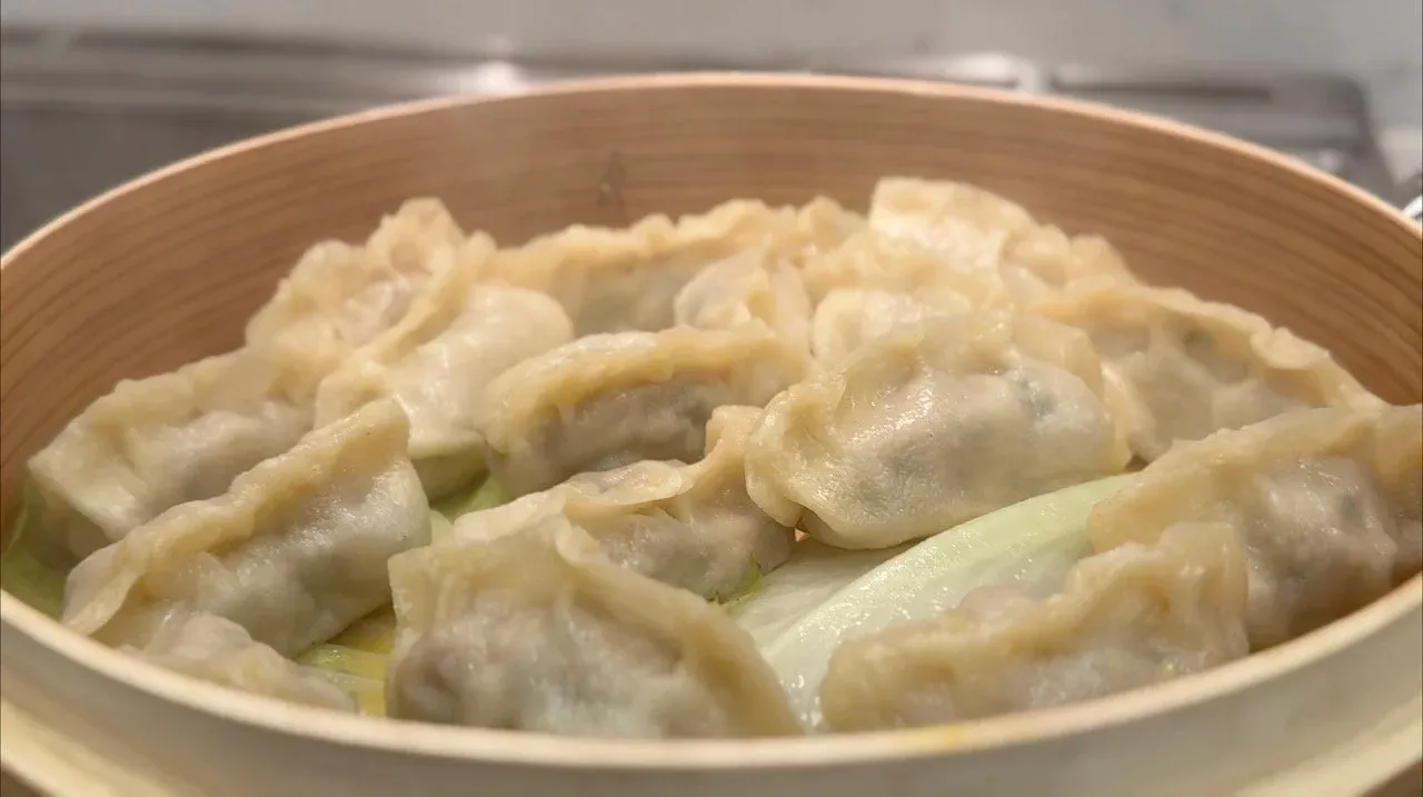 Steamed chicken momos in a bamboo steamer basket, showing the shiny, translucent dough with pleated tops.