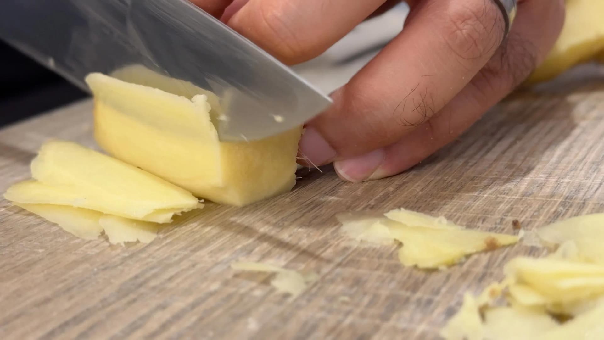 Slicing fresh ginger into thin pieces on a wooden cutting board with a sharp knife.