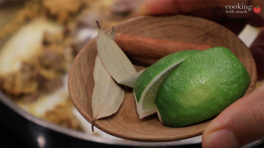 Wooden bowl holding sliced shallots and a fresh green lime for Balinese beef rendang ingredients.
