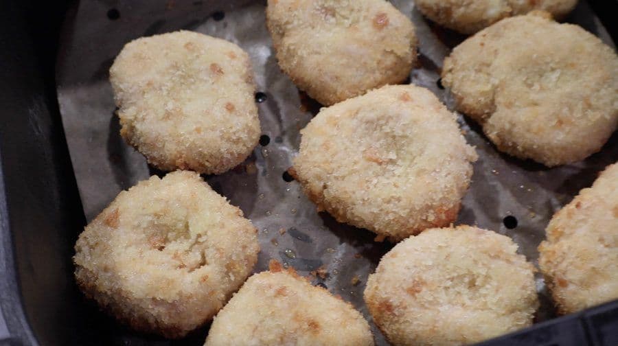Golden, crispy air fryer chicken nuggets in a black air fryer basket, cooked until golden brown.