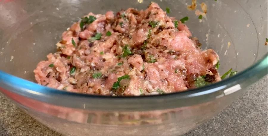 Raw homemade sausage patty mixture with bacon, onions, parsley, and seasonings in a glass bowl.
