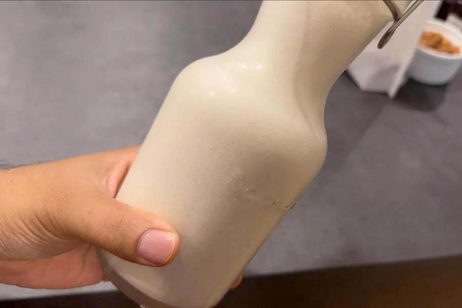 Hand holding a bottle of separated homemade almond milk before shaking.