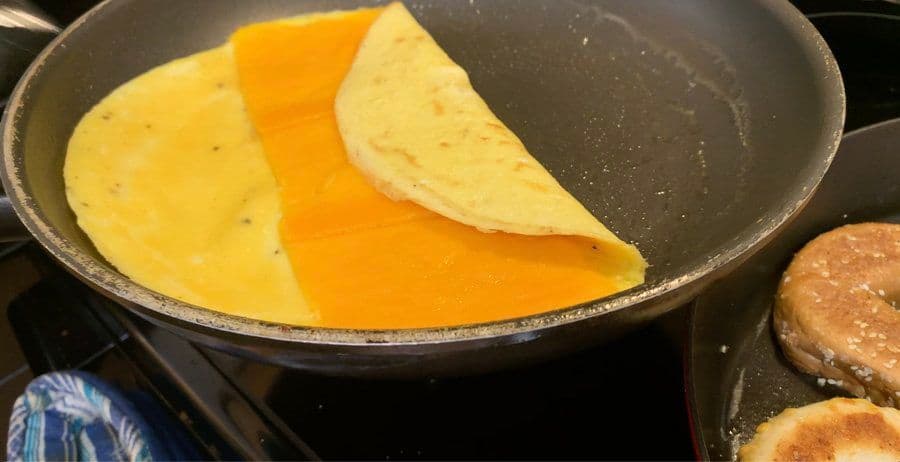 Omelet with melted cheese in the center being folded into a rectangle in a nonstick skillet