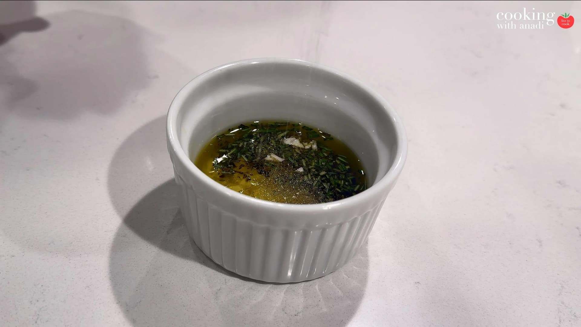 Small white ramekin filled with olive oil, minced garlic, chopped thyme, rosemary, and black pepper.
