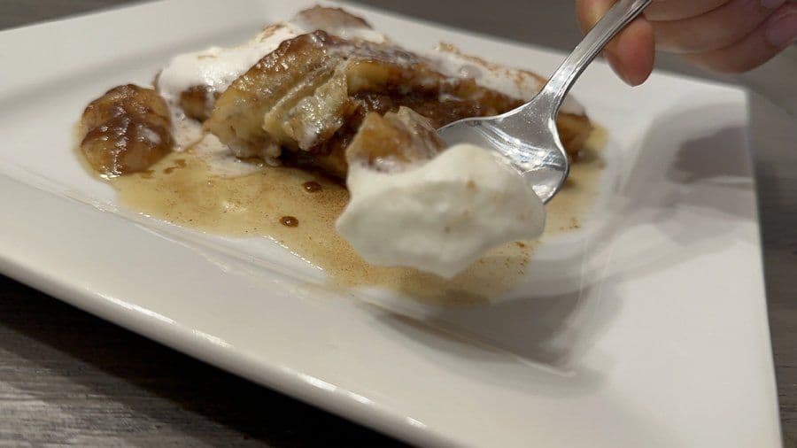 Caramelized bananas with whipped cream and cinnamon on a white plate with a fork.