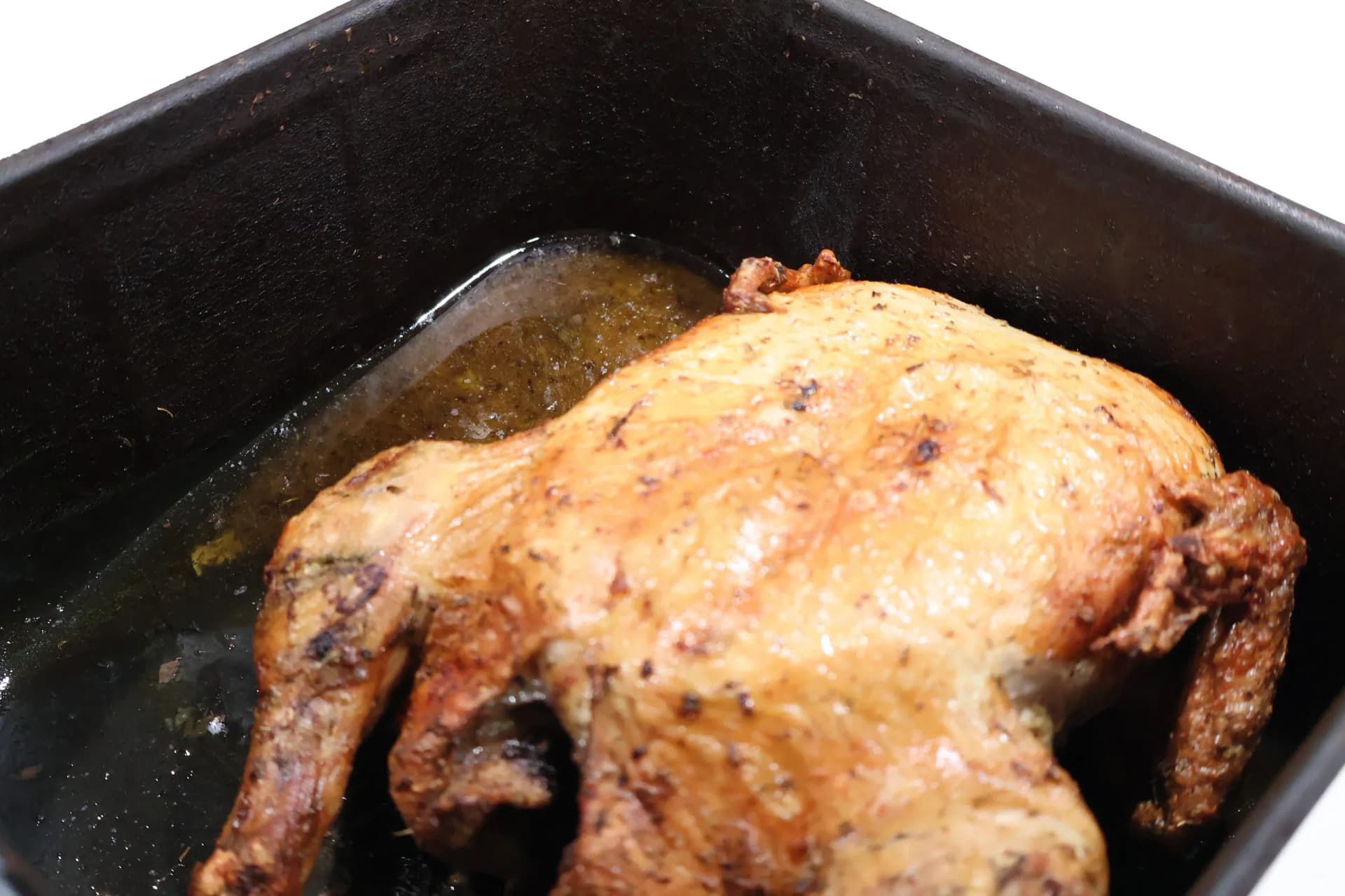 Cooked whole chicken resting in the black air fryer basket with the pan juices pooled around it.