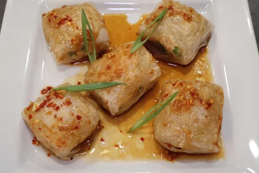 Five golden air fryer chicken dumplings in sauce, garnished with red pepper flakes and green onions on a white plate.