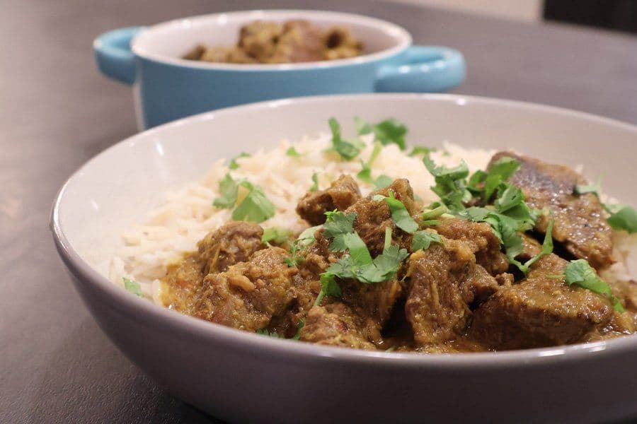 Balinese beef rendang served over rice noodles, garnished with fresh cilantro in a white bowl.