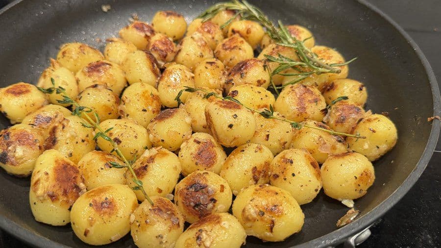 Butter and garlic herb sautéed baby potatoes in a skillet with golden-brown edges and fresh rosemary sprigs.