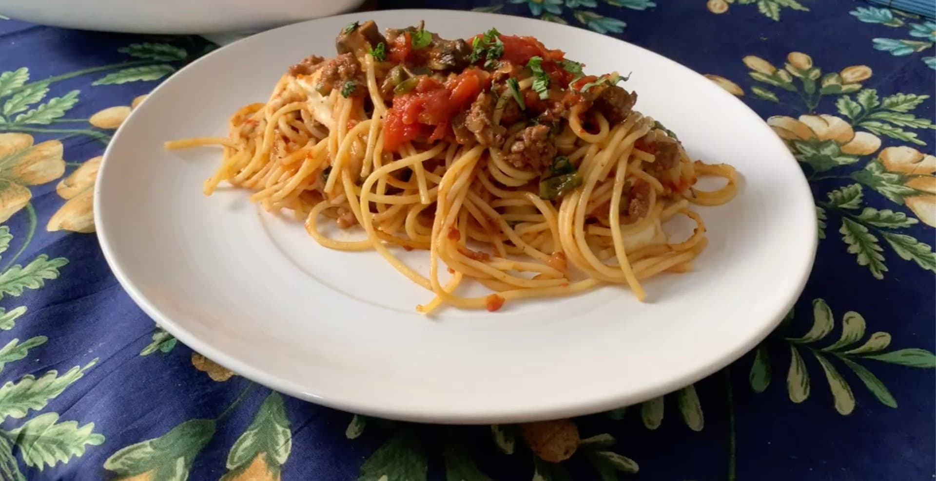 Spaghetti with meat sauce and diced tomatoes served on a white plate