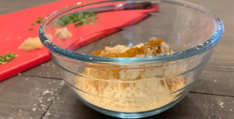 Besan flour batter mixed with spices in a glass bowl, ready for paneer pakora preparation.