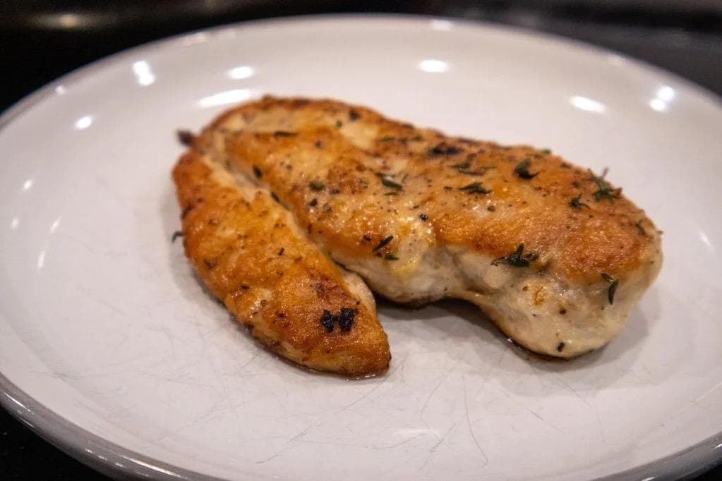Two golden-brown pan-fried chicken breasts seasoned with garlic and thyme on a white plate.