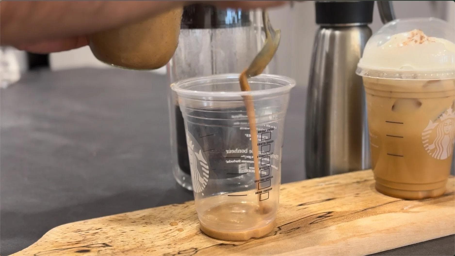 Espresso being poured into a clear cup with pumpkin sauce at the bottom, next to a finished iced latte.
