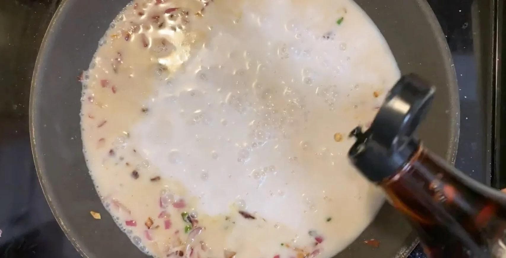 Coconut milk sauce simmering in a pan with visible chopped onions and spices, being stirred with a wooden spoon.