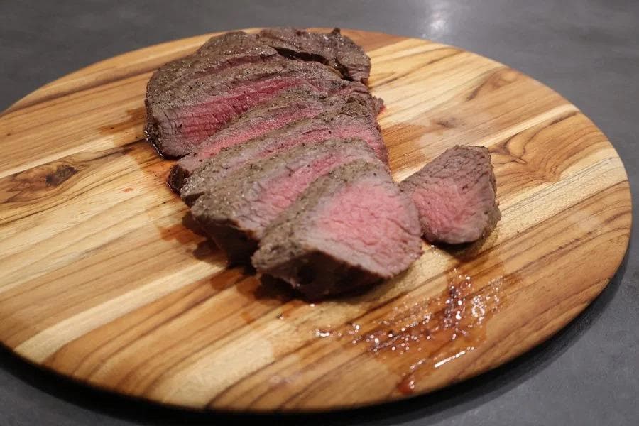Sliced air fryer sirloin steak with medium-rare pink center on wooden cutting board with sea salt.