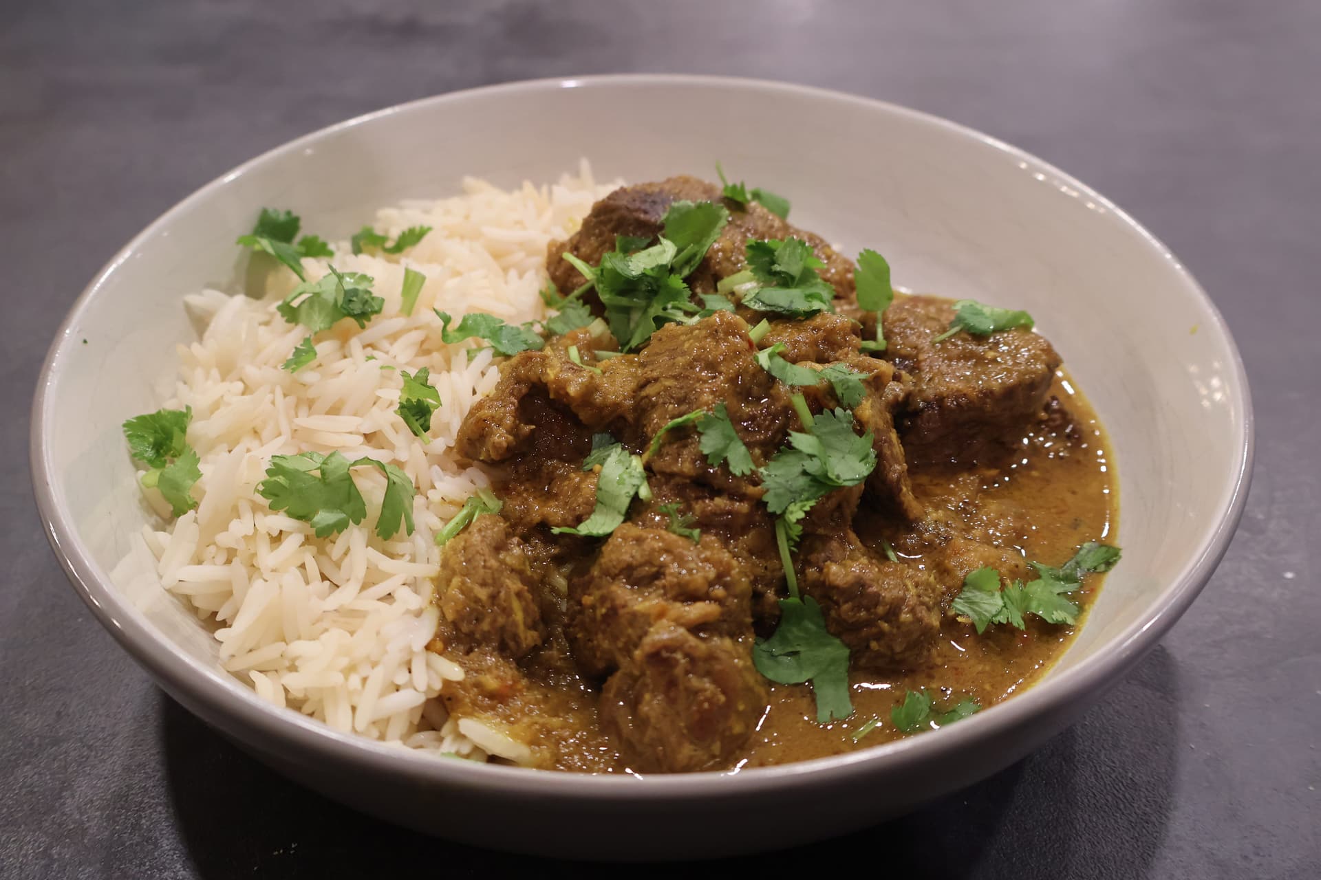 Beef rendang curry with rice, garnished with fresh cilantro in a white bowl.