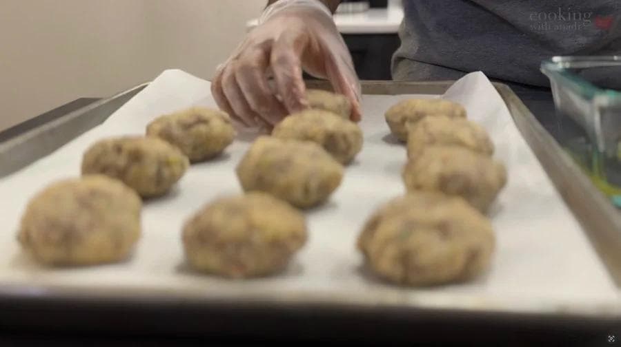 Hand placing uncooked perkedel potato fritters on parchment paper before frying.