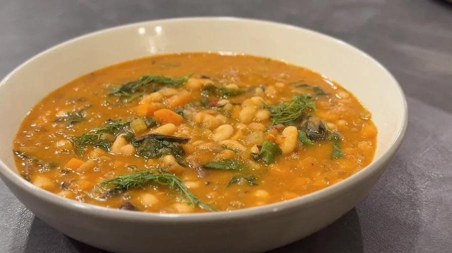 White bean and harissa stew garnished with fresh dill and wilted chard in a white bowl.
